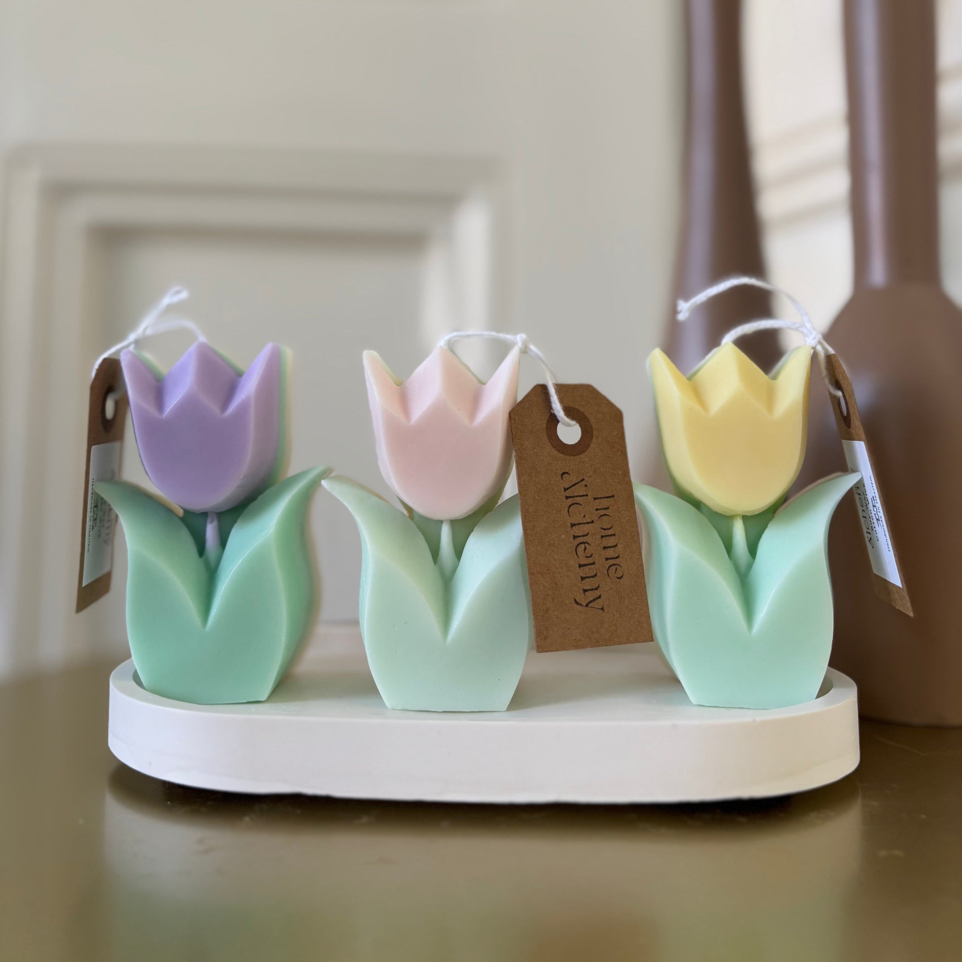 Three pastel tulip candles in soft pink, purple, and yellow — unscented, soy wax